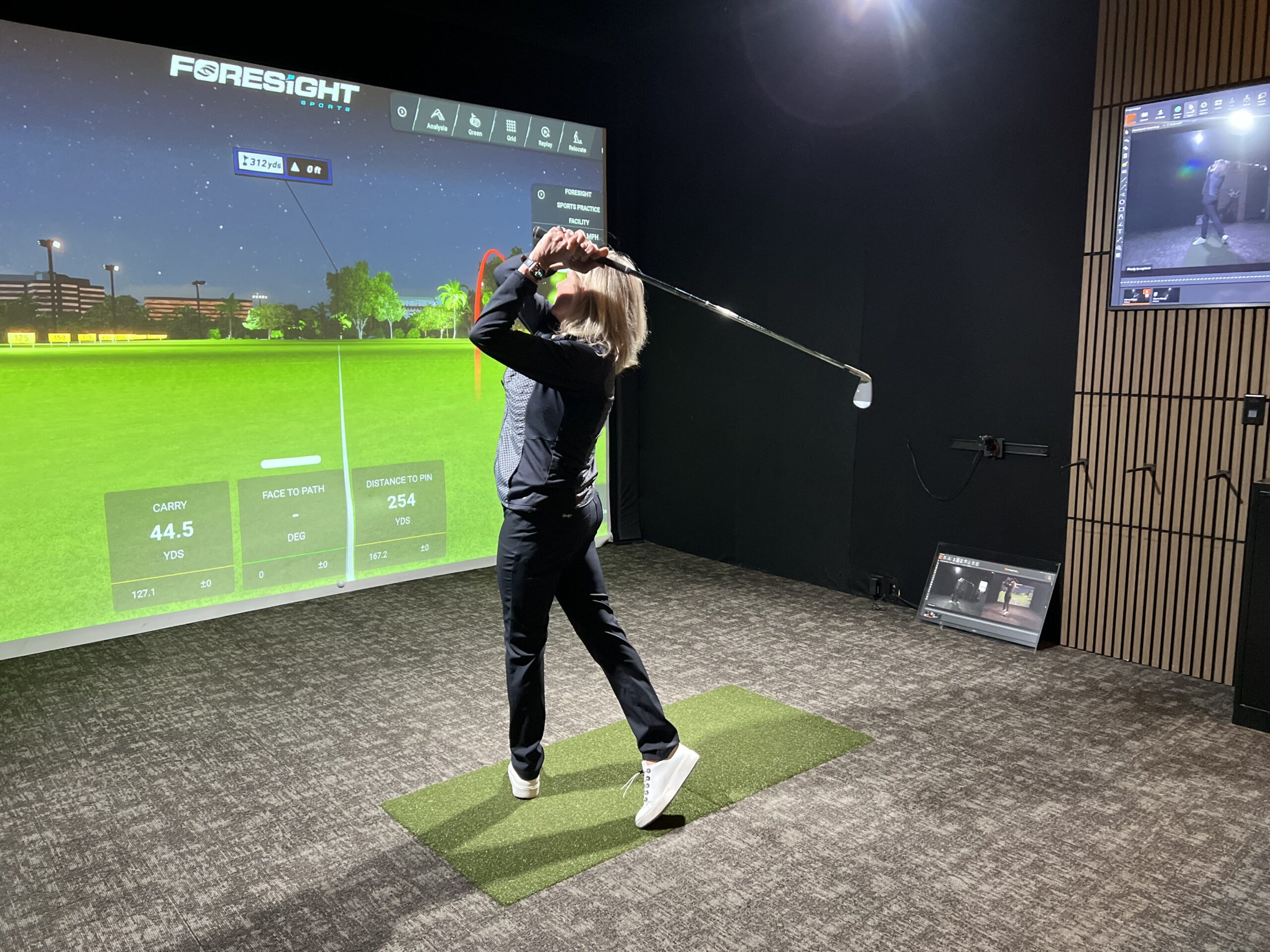 Golfer finishing a swing in front of a Foresight simulator screen in Weir Bay at The Loft, Lago Golf