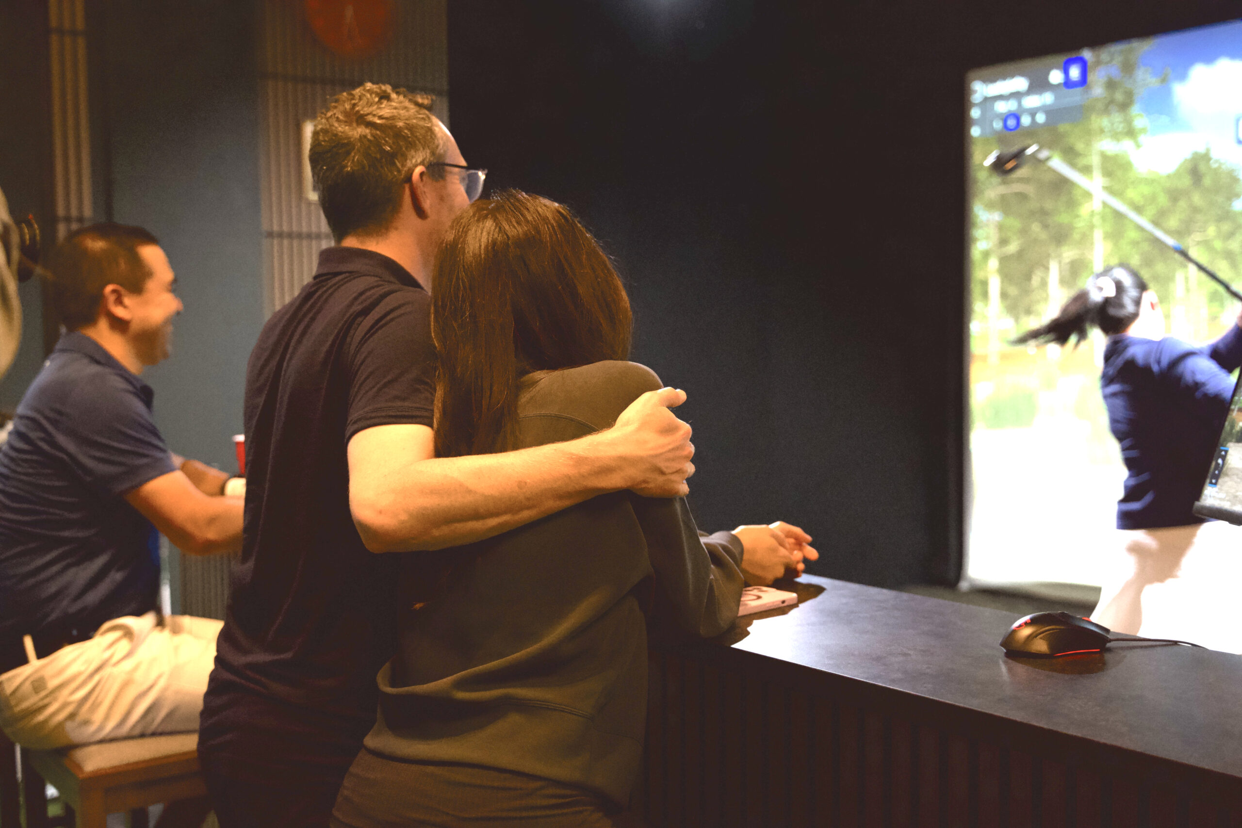 Adult couple hugging and smiling while enjoying indoor golf simulator play at Lago Golf