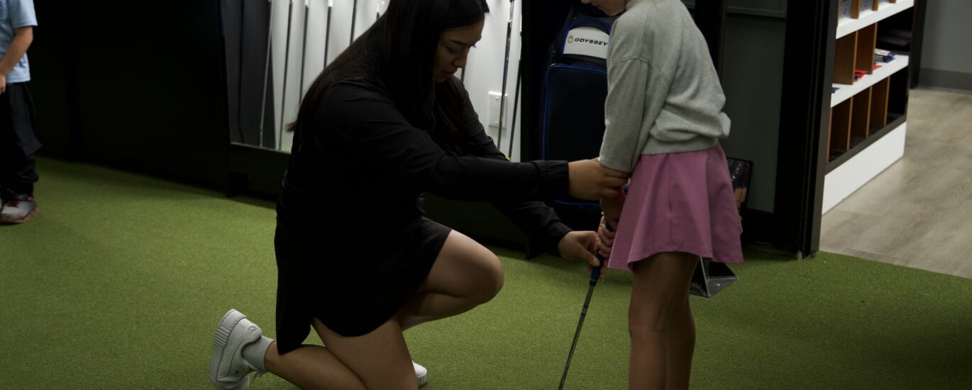 Golf instructor helping a young girl golfer with her grip during a girls-only junior lesson at Lago Golf