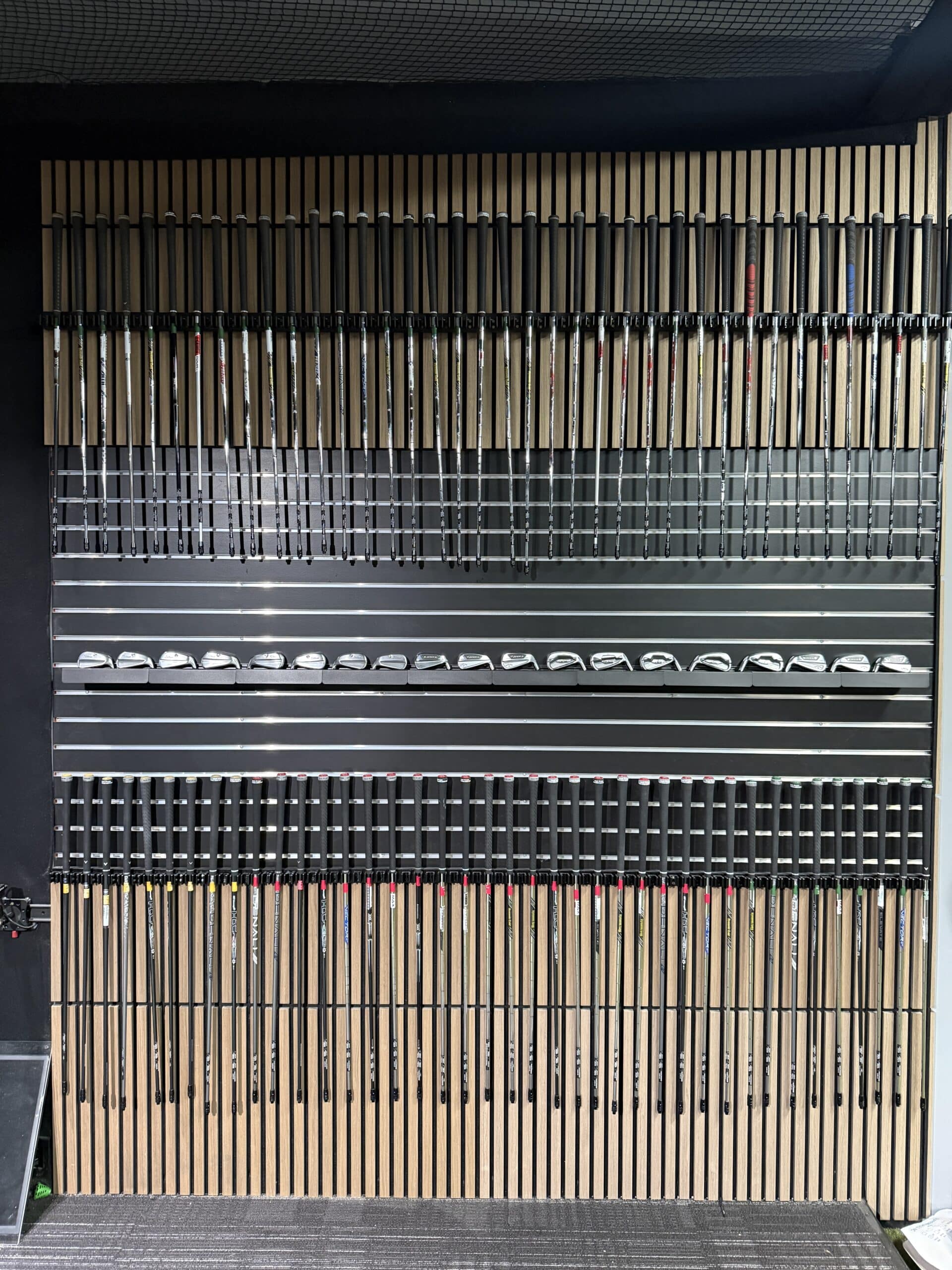Wall of golf clubs organized by shaft type and length, with wooden-looking shafts and metal clubheads lined up in rows.