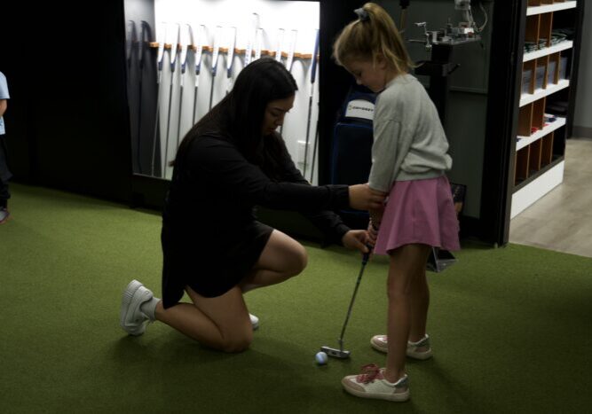 Golf instructor helping a young girl golfer with her grip during a girls-only junior lesson at Lago Golf